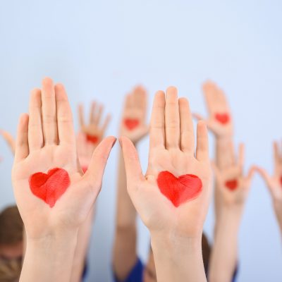 Raised in air hands with drawn hearts on palms against light background. Volunteering concept